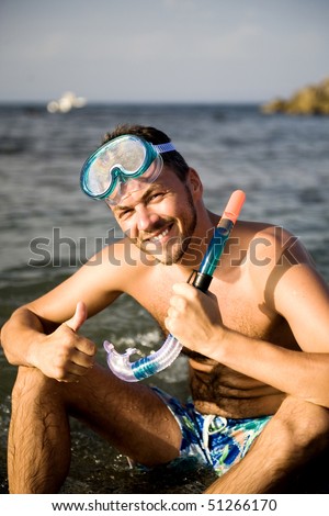 Young happy handsome summer diving man with swimming mask and snorkel preparing to dive in blue sea