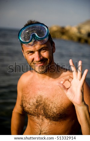 Young happy handsome summer diving man with swimming mask and snorkel preparing to dive in blue sea