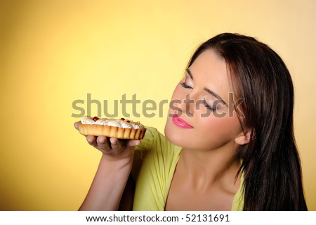 young beautiful girl eating small sweet cake. yellow background