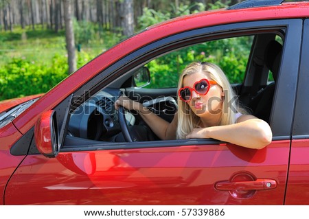 beautiful funny woman in heart shaped glasses in red shiny car outdoors