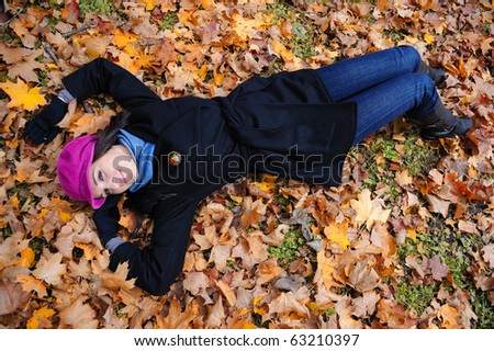 Pretty autumn girl relaxing outdoors in the forest on the fallen leafs