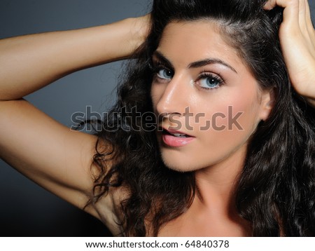 Beauty portrait of pretty woman with pure skin and natural make-up holding her black curly hair up and smiling