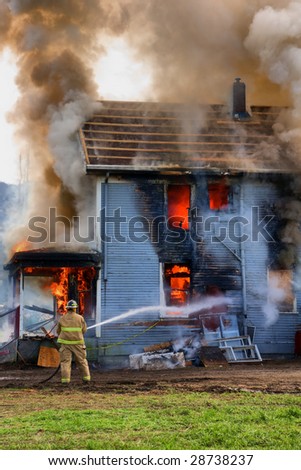 A single fireman fires his hose towards a burning house