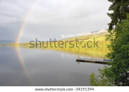 rainbow forms over a calm forested  lake