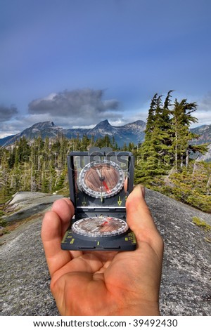 An orienteering compass is pointed towards a distant mountain summit to determine a bearing in degrees.