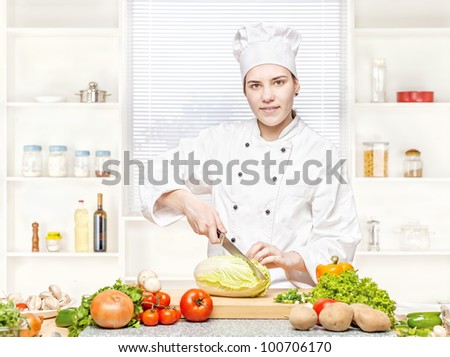 Young female chef cutting cabbage on the cutting board in kitchen