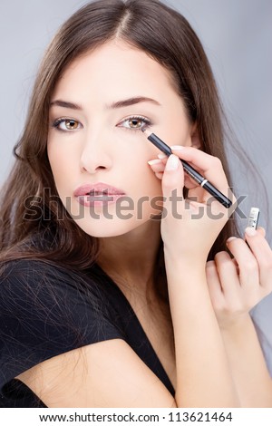 applying cosmetic pencil on woman's eye