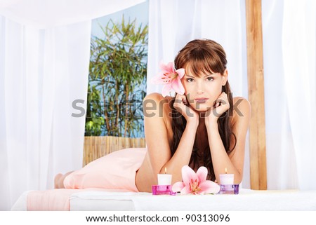 Pretty brunette woman with flower in her hair laying and resting in spa salon