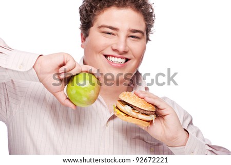 stock photo Young chubby man holding apple and hamburger