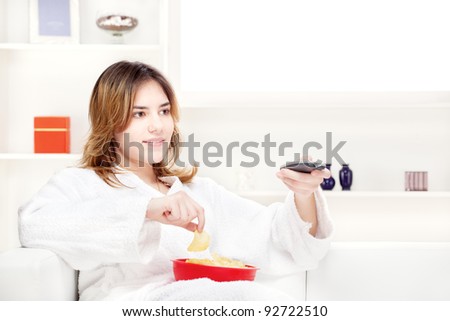 teenager girl at home eating chips and holding remote control