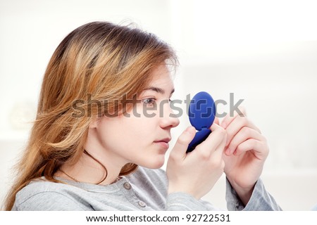 teenager girl looking in the mirror and checks pimples on face