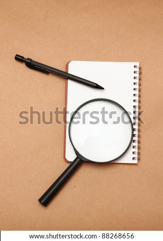 Blank reporters notebook and pencil on a brown paper background,magnifying glass
