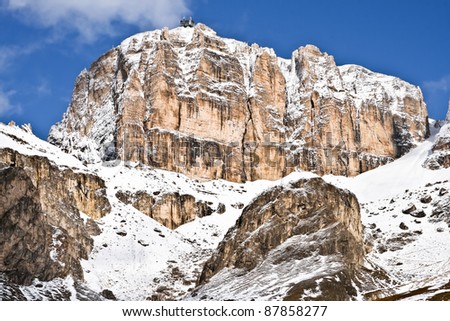 The picture represents a rocky and snow mountain. On the top there is a cableway.