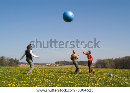 Three young people playing with big ball on the spring meadow