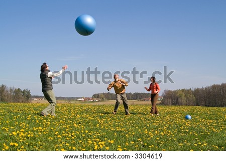 Three young people playing with big ball on the spring meadow