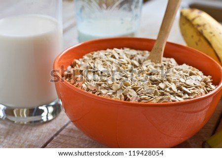 Oat flakes in orange bowl with banana and milk on wooden table. Selective focus.
