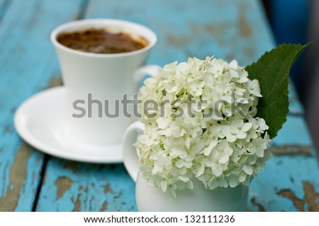 Bunch of bright white hydrangea flowers in vase on blue wooden background with cup of coffee