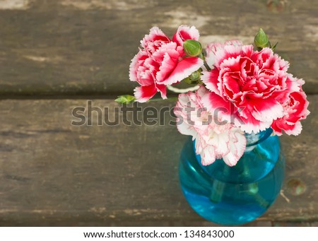 Bunch of fresh pink and white carnations in blue vase on wooden  background. Selective focus.
