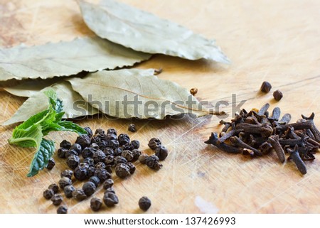 Different dry seasonings (bay leaf, black pepper, allspice) on wooden background. Selective focus.