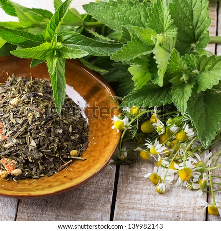 Dry herbal tea on plate on wooden background. Fresh melissa, mint, camomile. Selective focus. Square image.