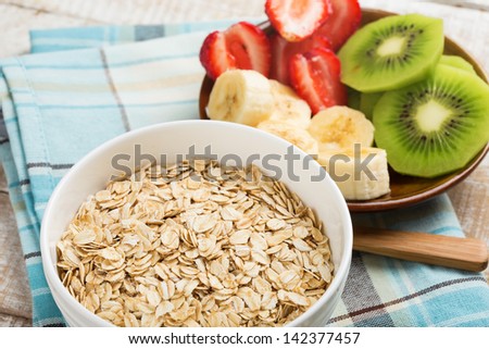 Oat flakes in orange bowl with banana, kiwi and strawberry. Selective focus.