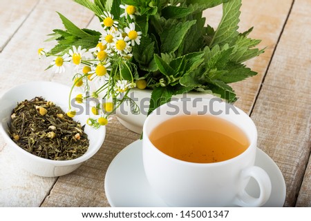Cup of tea. Dry herbal tea on plate on wooden background. Fresh melissa, mint, camomile. Selective focus.