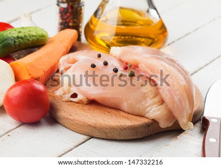 Fresh chicken meat on wooden board on white table with vegetables. Selective focus. Rustic style.