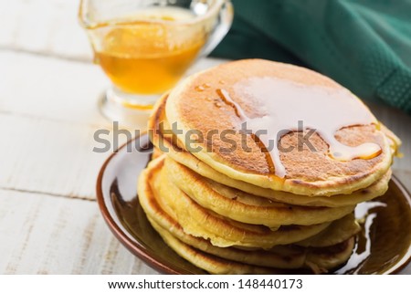 Appetizing pancakes on plate with honey/syrup on white table. Healthy breakfast. Selective focus.