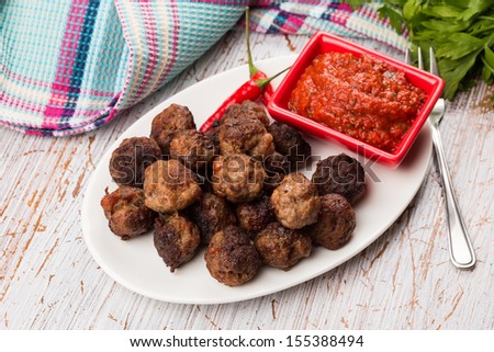 Meat balls on white plate with hot tomato sauce on wooden background. Selective focus.