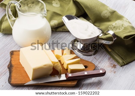 Fresh butter on wooden board, milk, sour cream  on white table. Selective focus. Rustic style.