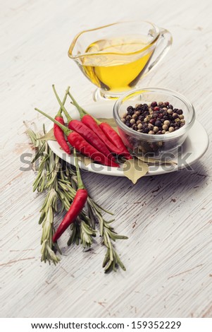 Fresh chili peppers, rosemary, bay leaves, black pepper, olive oil on wooden background. Selective focus.