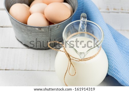 Milk in pitcher and eggs on white wooden table. Selective focus.