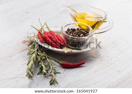 Fresh hot chili peppers, black peppers, rosemary, oil, bay leaves om white wooden background. Selective focus.