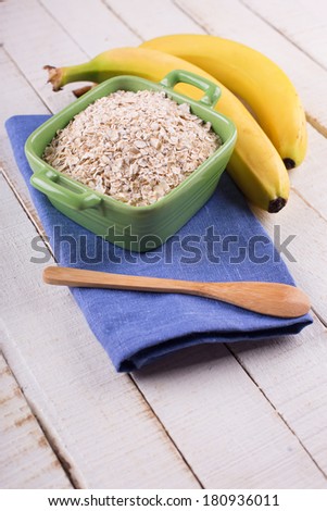 Oat flakes in orange bowl with bananas on wooden table. Selective focus.