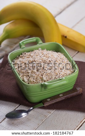 Oat flakes in orange bowl with banana  on wooden table. Selective focus.