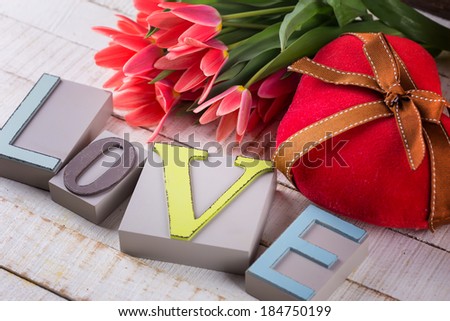 Postcard with fresh flowers tulips, heart and word love on white wooden background. Selective focus.