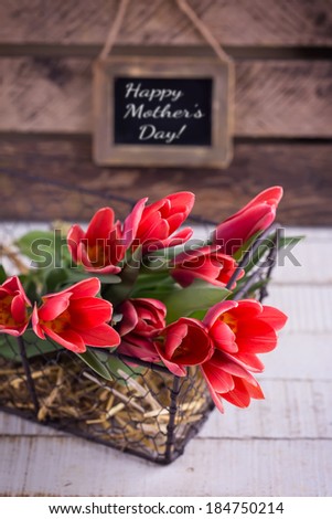 Postcard with fresh tulip flowers in bucket on wooden background. Happy Mother\'s Day on tag. Selective focus.