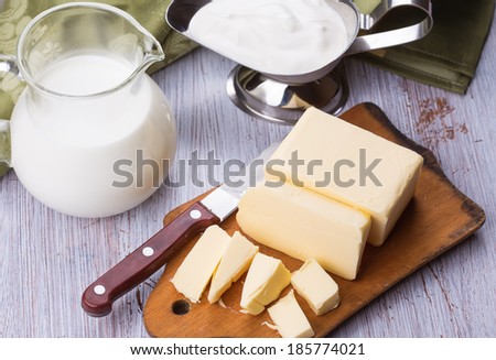 Fresh butter on wooden board, milk, sour cream  on white table. Selective focus. Rustic style.