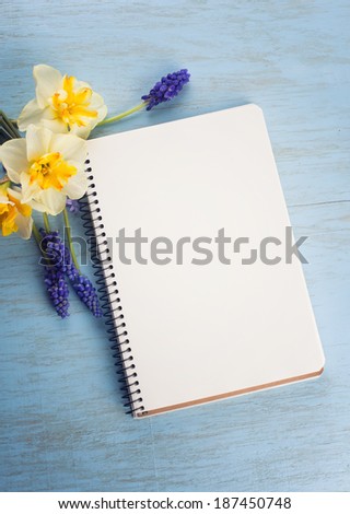 Notepad on wooden background with flowers daffodils and muscaries.