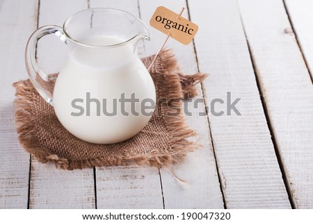 Fresh dairy products - milk in pitcher on wooden background. Tag with word organic. Selective focus, horizontal. Rustic style. Bio/organic/natural ingredients. Healthy eating.