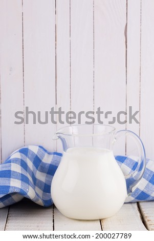 Milk or kefir in pitcher on white wooden table. Selective focus.