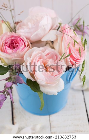 Postcard with fresh summer roses in bucket on white wooden background. Selective focus, vertical.