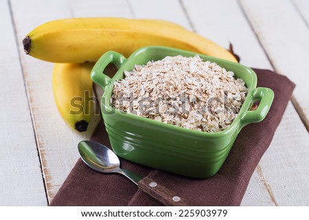 Oat flakes in bowl with bananas  on wooden table. Selective focus.