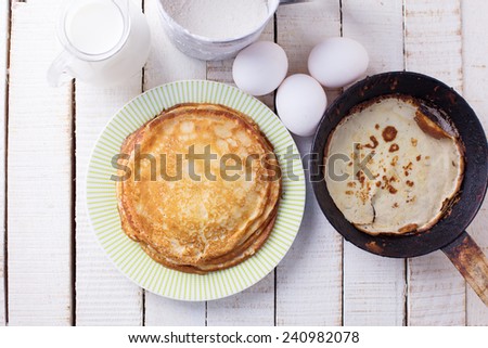 Pancakes and ingredients for it - eggs, flour, milk on white wooden background. Selective focus.
