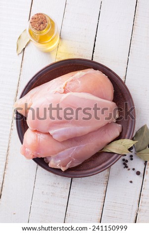 Fresh raw chicken meat on plate on white table with whole pepper, oil. Selective focus.