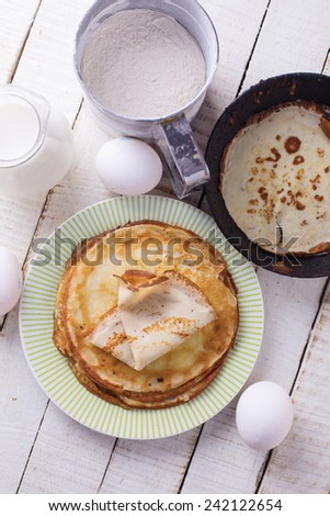 Pancakes and ingredients for it - eggs, flour, milk on white wooden background. Selective focus.