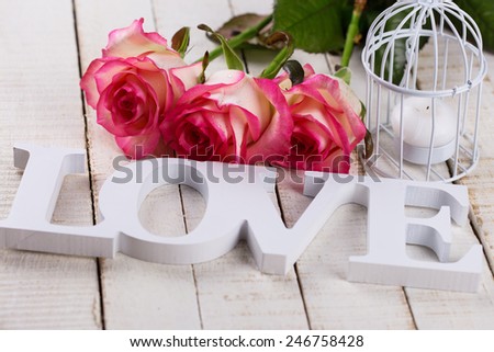 Background with fresh flowers and word love. Roses on white wooden table. Selective focus.
