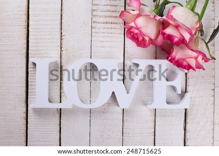 Background with word love  and fresh flowers. Roses on white wooden table. Selective focus.