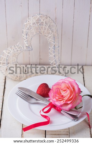 Romantic table setting. White plates, fresh rose and little red heart.  Selective focus is on flower