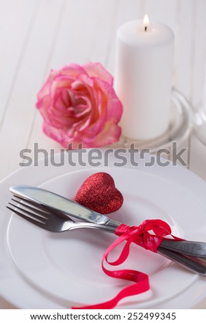 Romantic table setting. White plates, fresh rose, candle and little red heart.  Selective focus